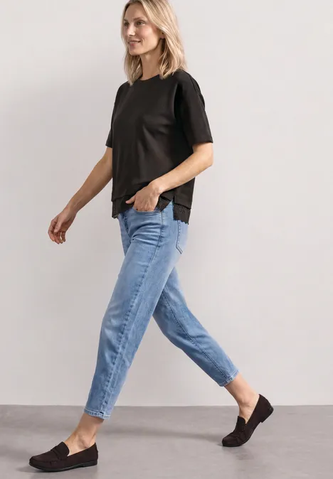 Eine Frau in schwarzem T-Shirt, blauen Jeans und schwarzen Slippern geht seitlich.