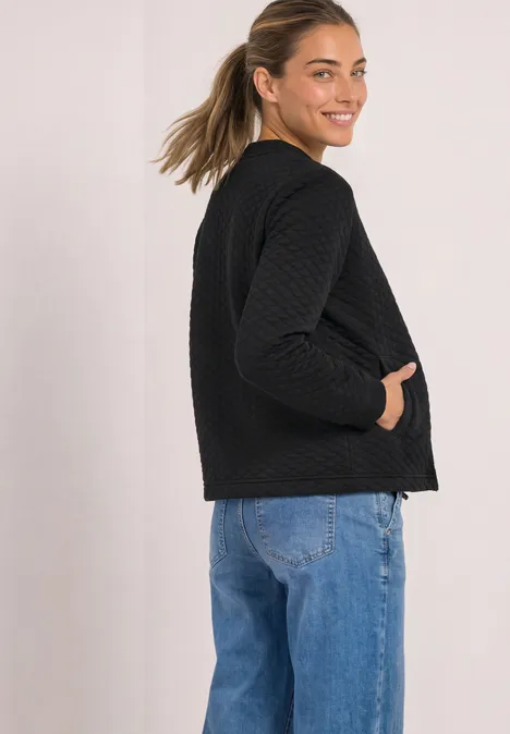Jasje met ronde hals en structuur Black Zijaanzicht van een vrouw in een zwarte doorgestikte jas en blauwe jeans, glimlachend over haar schouder.