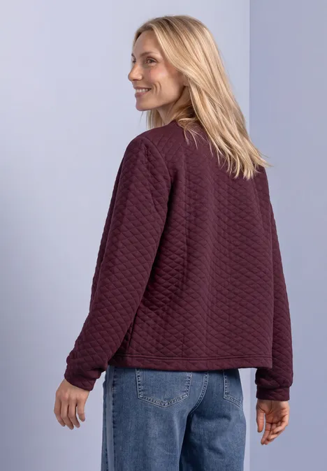 Jasje met ronde hals en structuur rustic rouge Een vrouw met blond haar draagt een kastanjebruine doorgestikte jas en spijkerbroek voor een lichte achtergrond.
