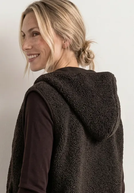 Teddy-Weste mit Kapuze und Zipper black coffee Blonde Frau mit Pferdeschwanz trägt schwarze, flauschige Kapuzenweste und lächelt über die Schulter.