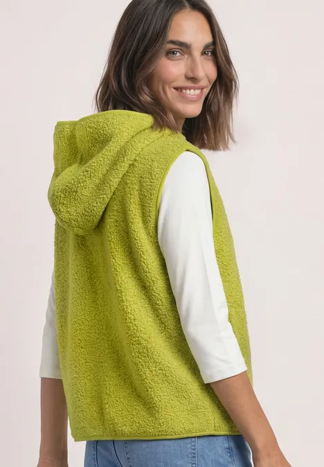 Vrouw draagt een limekleurige, zachte mouwloze capuchonvest op een witte top.