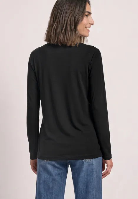 Frau von hinten in schwarzem Langarmshirt und blauen Jeans, schulterlanges Haar, lächelt seitlich