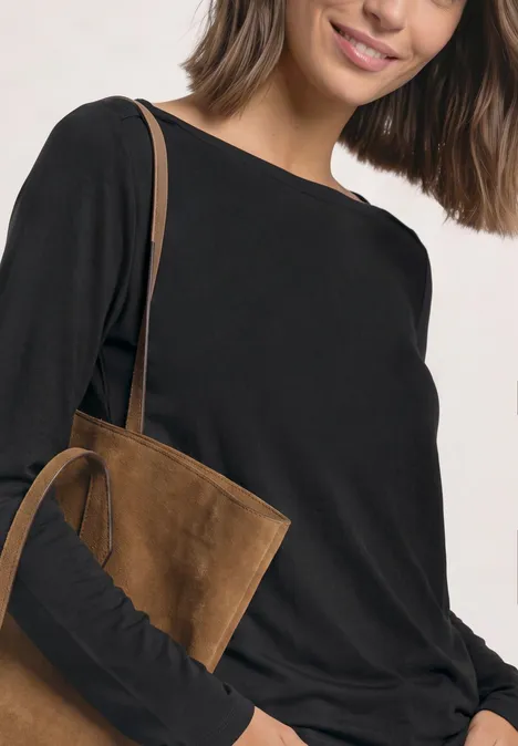 Frau in schwarzem Langarmshirt mit brauner Wildleder-Umhängetasche über der Schulter.