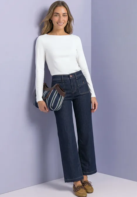 Bluzka Basic z dekoltem w łódkę off white Kobieta w białej bluzce z długim rękawem, ciemnych dżinsach i torbie na fioletowym tle.