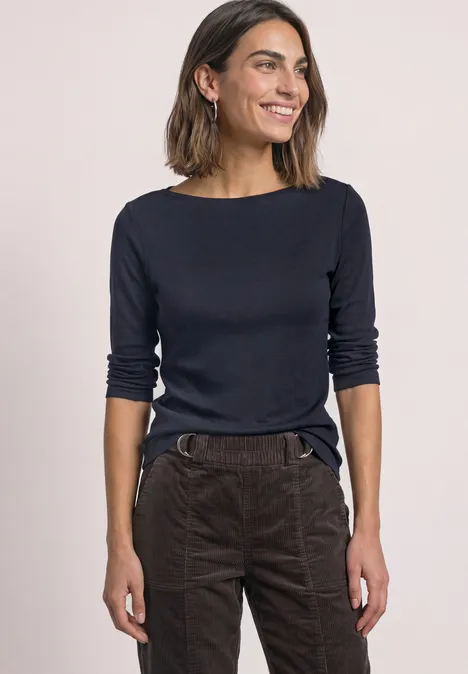 Frau in dunkelblauem Langarmshirt und brauner Hose lächelt entspannt.