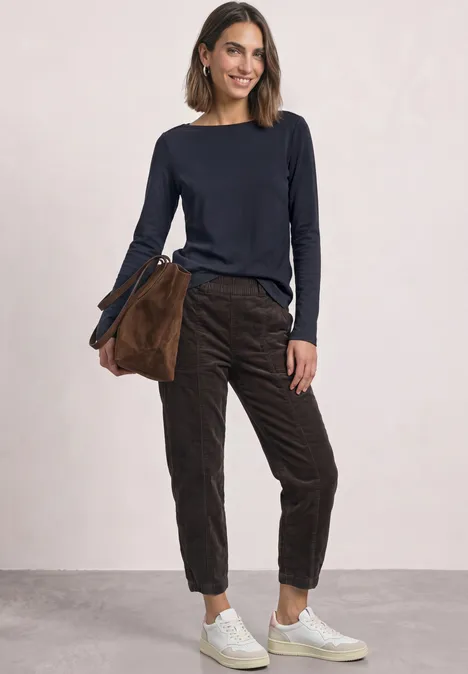 Frau in dunkelblauem Pullover, brauner Hose und weißen Sneakern mit passender brauner Tasche.