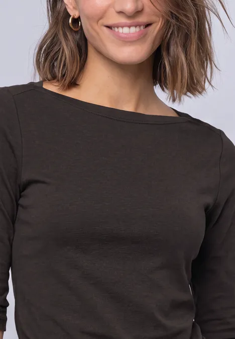 T-shirt basique à col bateau black coffee Eine Frau mit schulterlangem braunen Haar, goldenen Creolen und dunklem Langarmshirt lächelt freundlich.