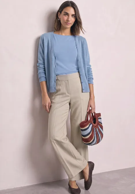 T-shirt basique à col bateau northern blue Frau in hellem Cardigan und Pullover, trägt beige Palazzohose und gemusterte Tasche, kombiniert mit dunklen Loafers.