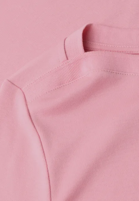 Close-up van een pastelroze T-shirt met zichtbare schoudernaad.