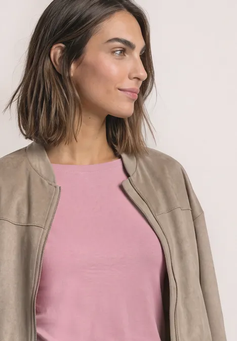 Een glimlachende vrouw met halflang haar draagt een roze top en een beige jasje, kijkt opzij.