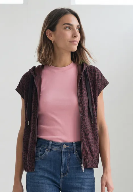 Frau in pinkem T-Shirt und gemustertem Cardigan, blickt seitlich.