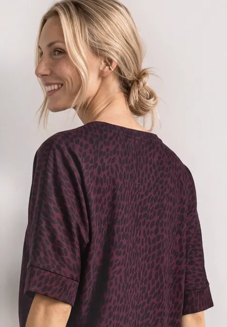 Batwing-shirt met ronde hals en print rustic rouge Blonde vrouw met opgestoken haar en glimlach, draagt een bordeauxrode top met zwart patroon, zijaanzicht.