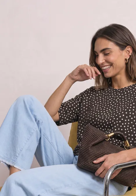 Batwing-shirt met ronde hals en print black coffee Lachende vrouw in gestippeld shirt en lichte jeans, met een gevlochten bruine tas.