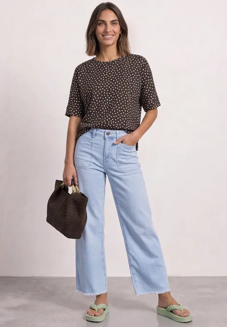 Batwing-shirt met ronde hals en print black coffee Vrouw in een shirt met stippen, lichtblauwe wijde jeans, groene sandalen en een bruine tas.