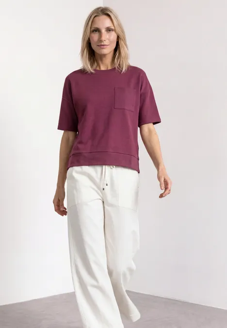 T-Shirt mit Rundhals und Struktur dark clouded blush Eine Frau posiert in einem weinroten T-Shirt und weißen, weiten Hosen vor weißem Hintergrund.