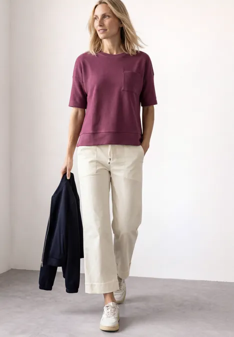 T-Shirt mit Rundhals und Struktur dark clouded blush Eine Frau trägt ein lila T-Shirt, helle weite Hosen und weiße Sneaker, in der Hand eine dunkle Jacke.