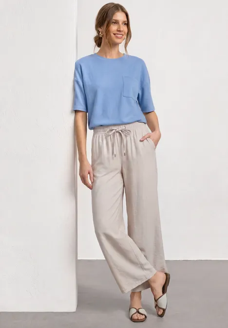 Shirt met ronde hals en textuur northern blue Vrouw in lichtblauw shirt en ruime beige linnen broek, sandalen, casual pose voor witte muur.