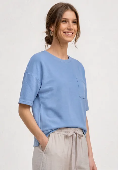 Shirt met ronde hals en textuur northern blue Een glimlachende vrouw in een blauw T-shirt en beige broek, handen in haar zakken.