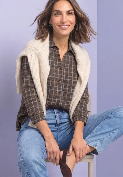 Shirt met 3/4-mouwen van jersey in blouse-stijl silk brown Een glimlachende vrouw zittend, met een bruin geruit overhemd, lichte trui over haar schouders en blauwe jeans.