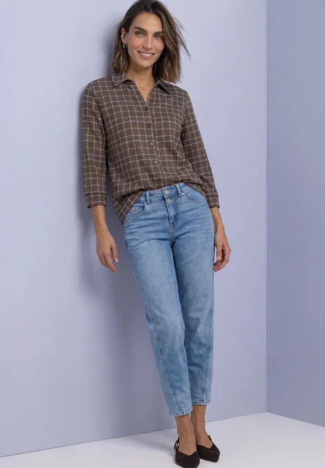 Shirt met 3/4-mouwen van jersey in blouse-stijl silk brown Vrouw in bruin geruiten blouse en lichtblauwe jeans voor paarse achtergrond.