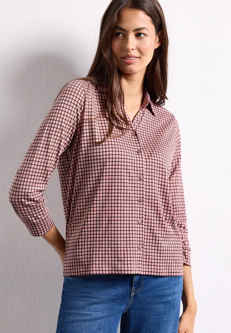 Shirt met 3/4-mouwen van jersey in blouse-stijl warm blush Eine Frau trägt eine rot-weiß karierte Bluse und blaue Jeans vor einer weißen Wand.