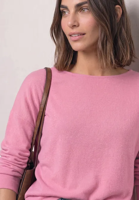 Koszulka z długim rękawem i elastycznym wykończeniem warm blush mel. Kobieta z brązowymi włosami w różowym swetrze i torbą na ramię, uśmiechnięta, patrzy w bok.