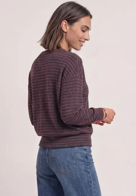 Femme de profil portant un pull rayé et un jean, souriante.