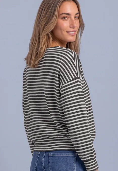 T-shirt à manches longues avec ourlet élastiqué black coffee mel. Eine junge Frau mit hellbraunem Haar trägt gestreiftes Langarmshirt und Jeans, schaut lächelnd über die Schulter.