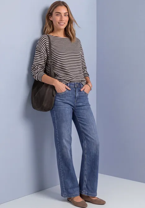 T-shirt à manches longues avec ourlet élastiqué black coffee mel. Frau steht vor hellblauem Hintergrund, trägt gestreiftes Shirt, blaue Jeans, braune Loafers und schwarze Schultertasche.