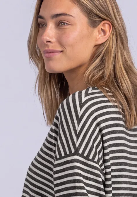 T-shirt à manches longues avec ourlet élastiqué black coffee mel. Eine junge Frau mit langem, hellem Haar trägt ein gestreiftes Oberteil und schaut seitlich lächelnd.