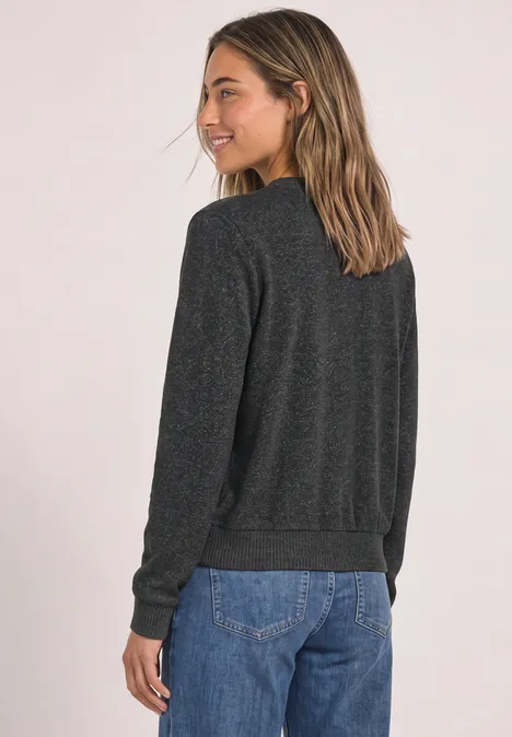 Frau im Profil mit grauem Pullover und blauer Jeans, lächelnd.