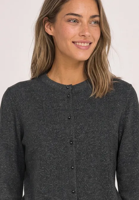 Eine lächelnde Frau in einer dunkelgrauen Strickjacke mit Knöpfen.
