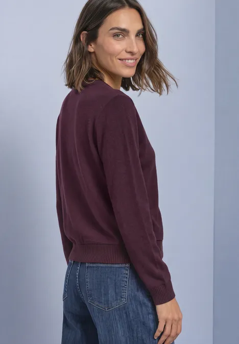 Frau in dunkelviolettem Pullover und Jeans schaut lachend über die Schulter.