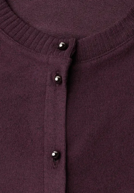 Nahaufnahme eines violetten Cardigans mit kleinen schwarzen Perlenknöpfen.