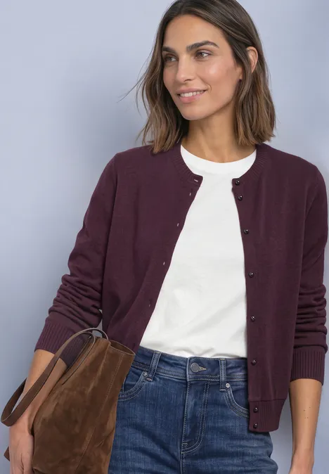 Frau in weißem T-Shirt, weinrotem Cardigan und Jeans trägt eine braune Wildledertasche