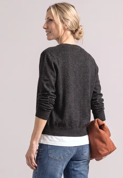 Femme vue de dos, pull noir, t-shirt blanc, chignon blond, jean, tenant un sac marron.