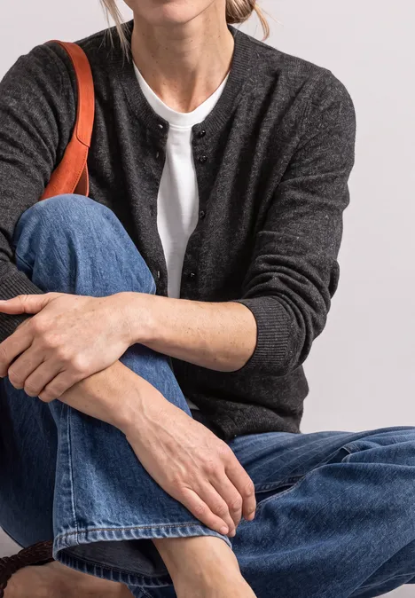 Femme en jean, t-shirt blanc et gilet gris foncé assise, main sur le genou, bandoulière de sac orange.