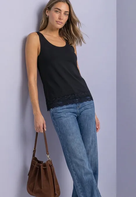 Femme portant un débardeur noir, un jean et un sac à main marron sur fond uni.