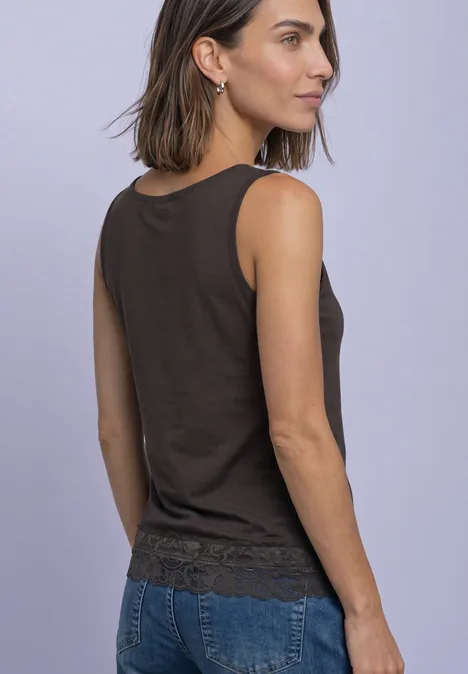 Femme vue de dos/profil portant un débardeur marron à dentelle et un jean bleu devant un mur violet pâle.