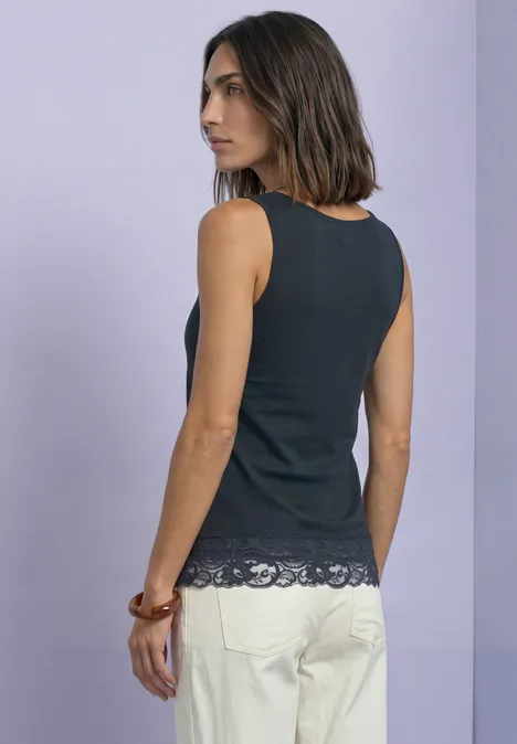 Femme en débardeur noir à dentelle et pantalon clair sur fond lumineux.