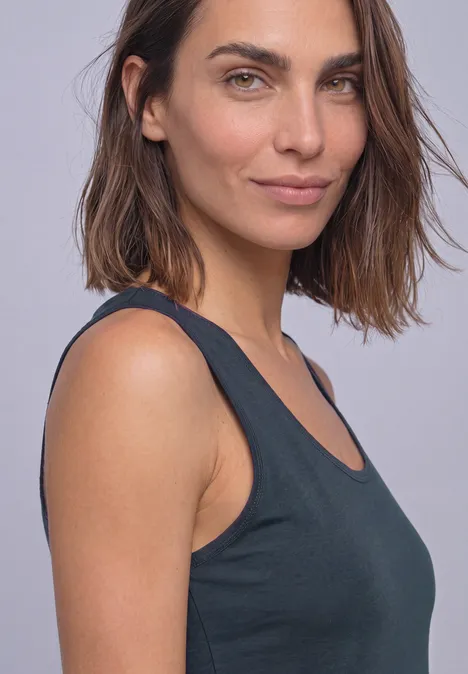 Portrait d’une femme aux cheveux bruns portant un top noir sans manches sur fond clair.