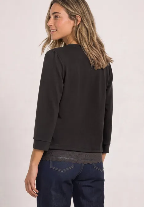 Eine Frau trägt seitlich ein schwarzes Sweatshirt mit 3/4-Ärmeln und lächelt.