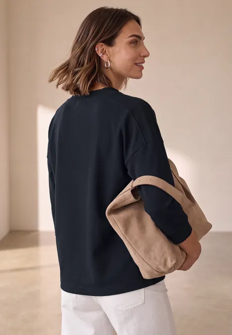 3/4-Arm Shirt mit Rippstrukturdetails indigo night Frau in schwarzem Pullover und weißer Hose hält eine beige Tasche vor minimalistisch hellem Hintergrund.