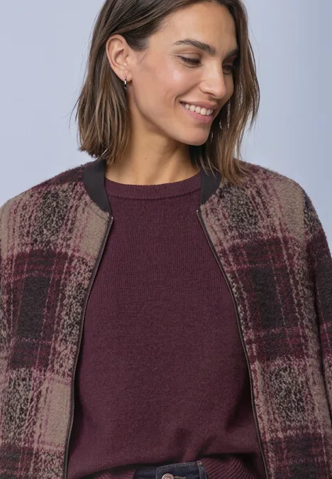 Frau lächelt und trägt einen bordeauxfarbenen Pullover und eine karierte Jacke.