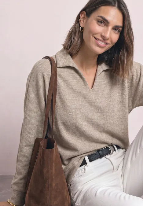 Femme souriante en pull beige, pantalon blanc et sac marron sur fond clair
