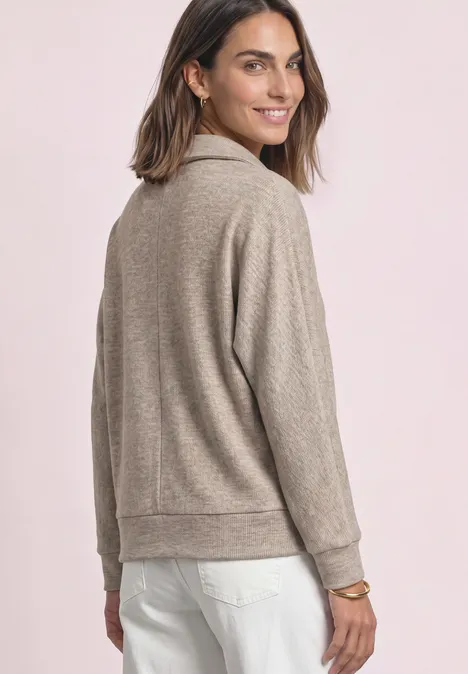 Femme portant un pull beige regardant par-dessus son épaule, souriante.