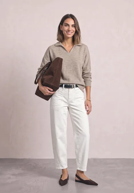 Femme en pull beige, pantalon blanc, ceinture noire, sac marron et chaussures plates.