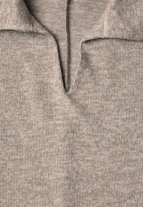 Gros plan d’un pull en maille beige à col montant et encolure en V, texture douce et épaisse.