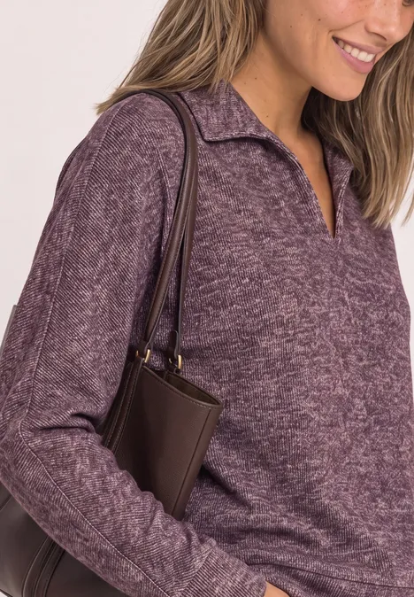Koszulka Polo z długim rękawem w stylu melanżowym rustic rouge mel. Kobieta w fioletowym swetrze i ciemnobrązowej torebce na ramieniu, lekko się uśmiecha.
