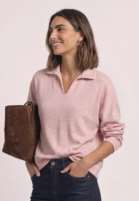 Koszulka Polo z długim rękawem w stylu melanżowym vintage blush mel. Kobieta w różowym swetrze z dekoltem V i brązową torbą, uśmiecha się z boku, ręce w kieszeniach